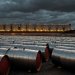 Barriles de crudo apilados y un petrolero al atardecer